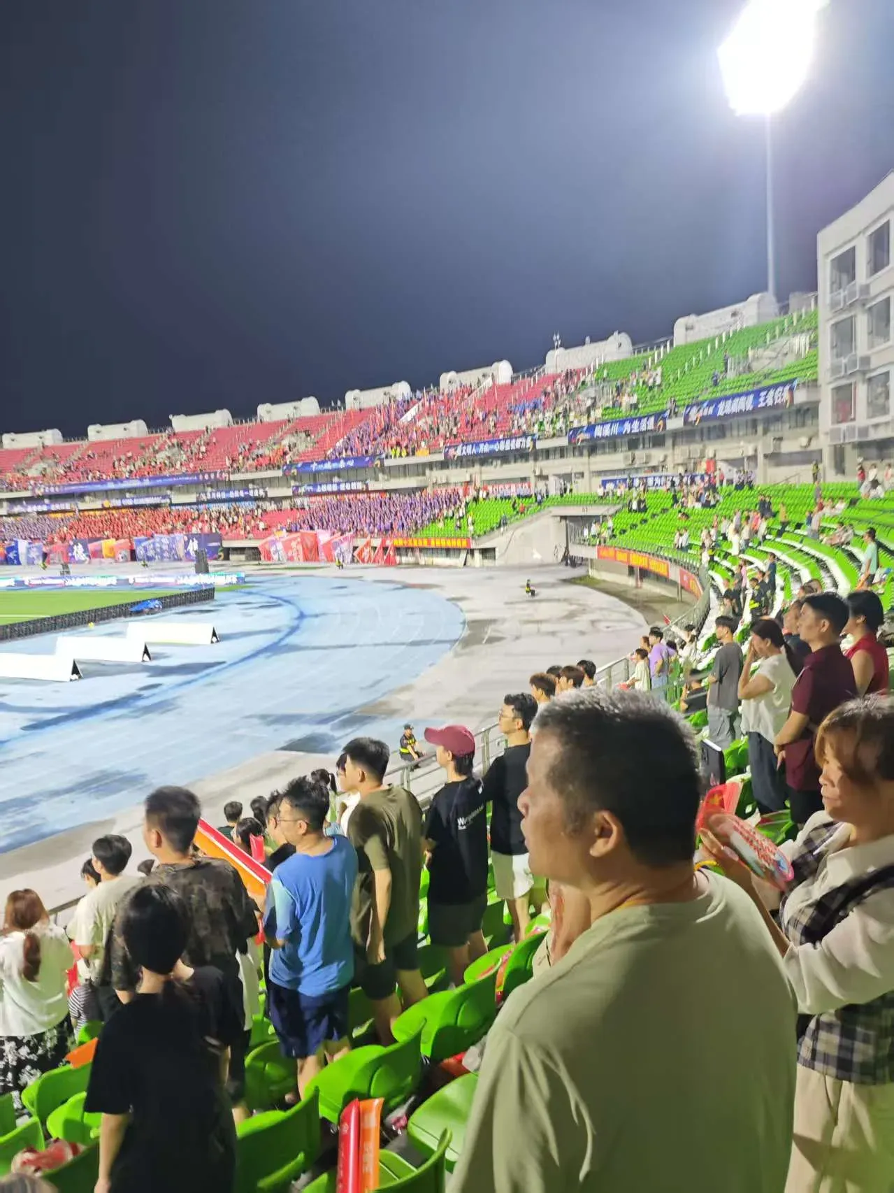 夜晚的赣超足球现场，观众站在红绿看台上助威