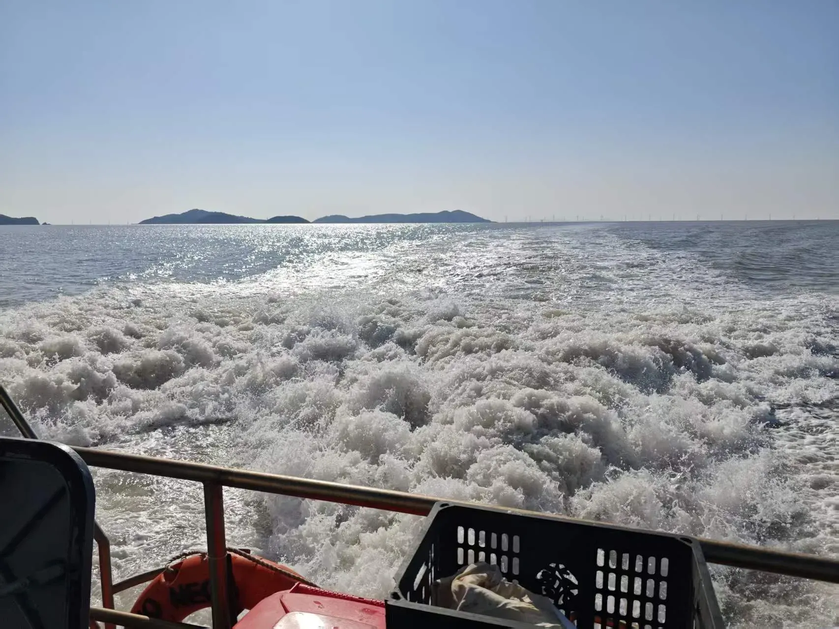 舟山船尾翻起白色海浪，远处有岛屿和晴朗天空